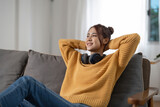 Happy smiling asian young woman in headphones listening to music lying on couch at home, people and leisure concept