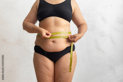 Cropped obese overweight woman with big cellulite sagging abdomen, measuring circumference of waist, belly with yellow roulette tape. Checking size before liposuction surgery. Show off adipose body © Юля Бурмистрова