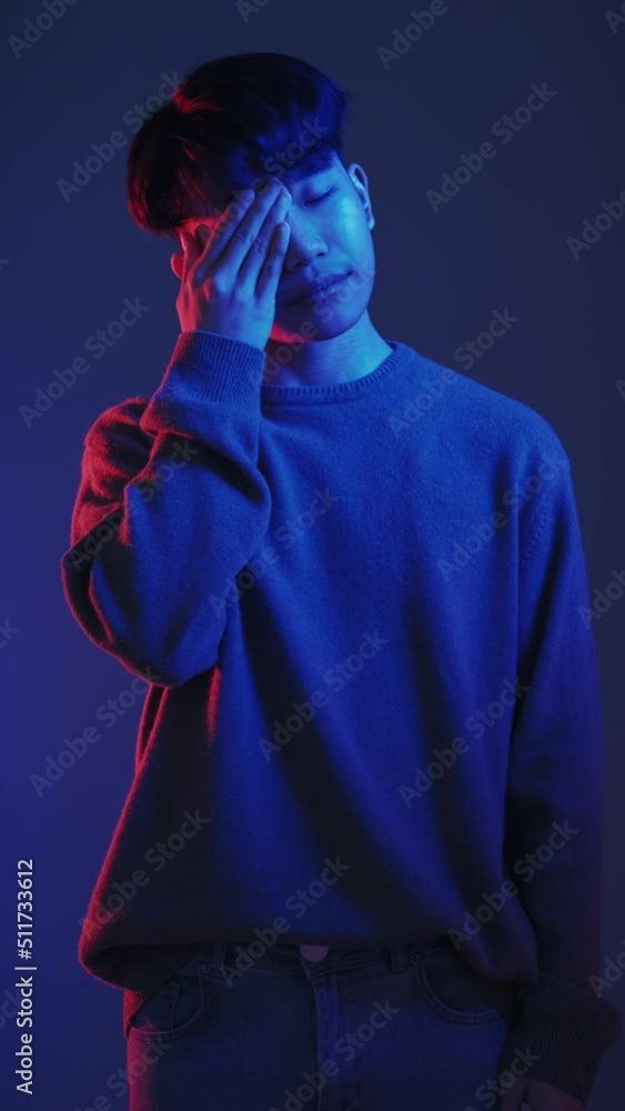 Sleepless night. Insomnia fatigue. Boring party. Red blue neon color light tired exhausted sleepy Asian guy yawning rubbing eyes isolated on dark vertical background. Sleepless night. Insomnia fatigue. Boring party. Red blue neon color light tired exhausted sleepy Asian guy yawning rubbing eyes isolated on dark vertical background.