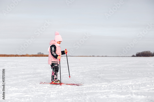 Little girl is learning to ski. Child in pink warm suit skiing in snow on frosty winter day, side view, snow background.