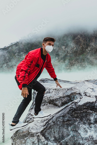 Foto young man in red bomber jacket climbing a rock at kawah putih sulfer lake