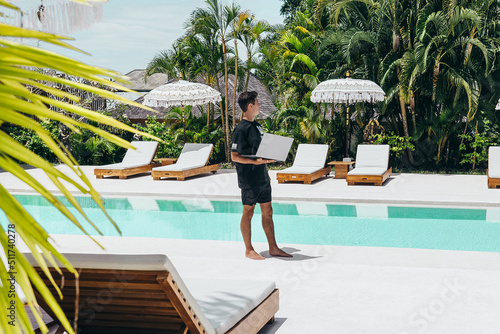 young digital nomad near tropical pool in bali with silver laptop computer © Alexander White