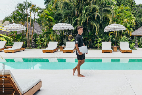 young digital nomad with silver laptop computer walking near tropical pool in bali © Alexander White