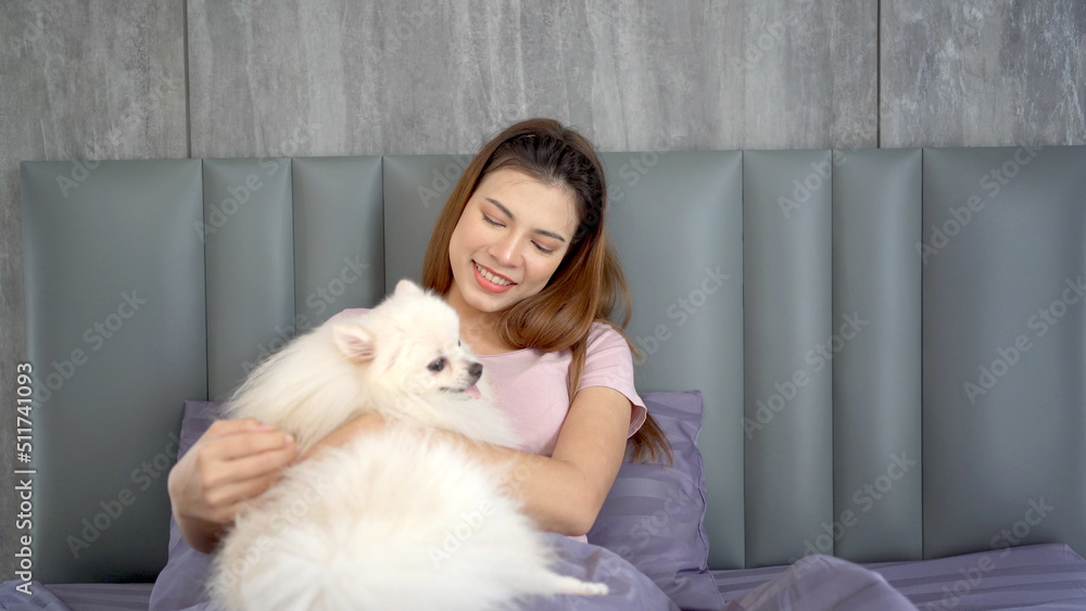 Beautiful Asian young woman enjoy playing with her pet, a Pomeranian on the bed. Beautiful Asian young woman enjoy playing with her pet, a Pomeranian on the bed.