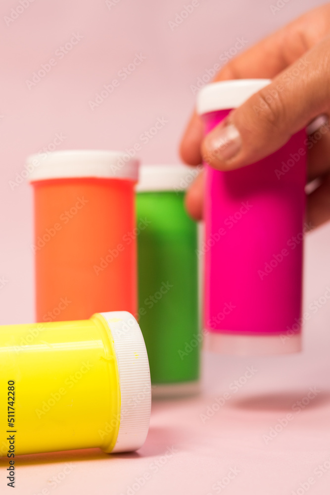 Hand taking a yellow neon paint and other neon paints on pink background Hand taking a yellow neon paint and other neon paints on pink background