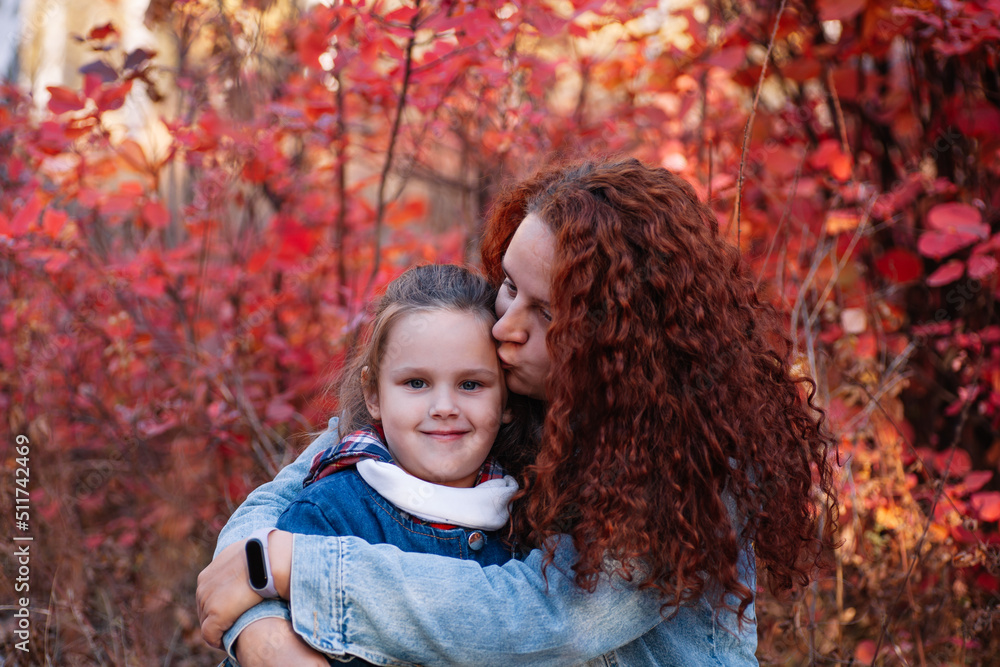 close up happy family concept. mother with long curvy hair kiss smiling girl on autumn forest background. happy motherhood. close up happy family concept. mother with long curvy hair kiss smiling girl on autumn forest background. happy motherhood.