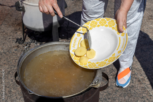 The cook drops potatoes from the plate into the cauldron in which fish soup is cooked