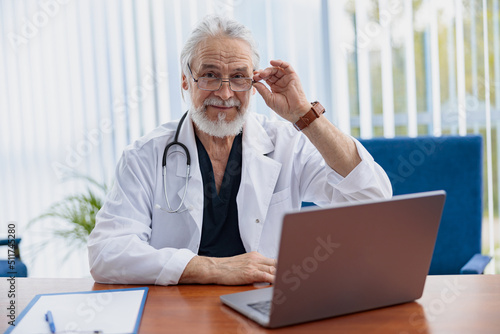 Doctor therapist in glasses with stethoscope using laptop while working at medicine office