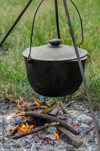 a pot in which soup is cooked on a tripod stands on a fire