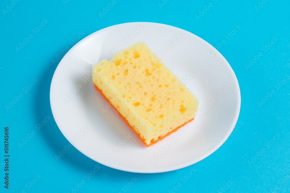 Sponge for washing dishes and cleaning in the apartment on a plate on a blue background. The concept of using environmentally friendly detergents for the home