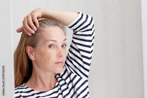 Beautiful 40s woman looking at gray hair in mirror reflection on growing out root photo
