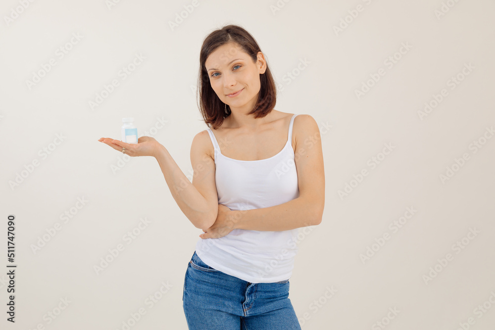 Portrait of young pretty woman with dark hair wearing white top, holding blue plastic bottle of pills for womans health. Portrait of young pretty woman with dark hair wearing white top, holding blue plastic bottle of pills for womans health.