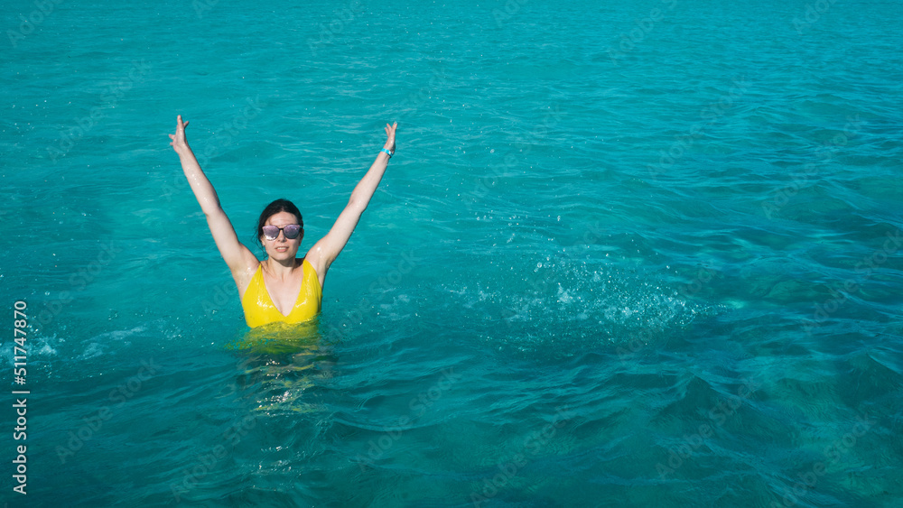 A young woman in a yellow swimsuit is bathing in the azure sea, beautiful clear water. Vacation on a tropical island