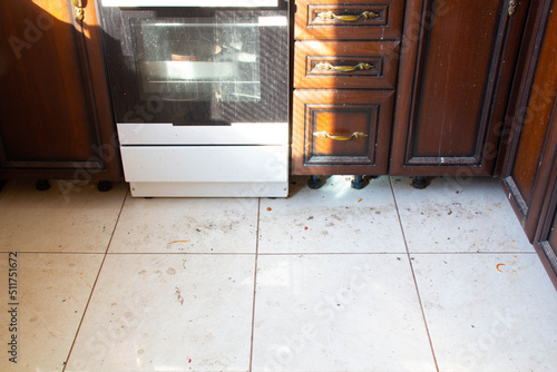 Dirty kitchen floor. Very dirty light tile floor in the kitchen. Unwashed gas stove and dirty kitchen furniture under the rays of the sun from the window. Frying pan, a baking dish in an electric oven
