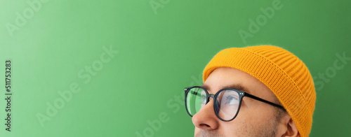 Close up face of young man with glasses and a hat looking at the left top side. Banner with copy space. The concept of choice, vision and searching photo