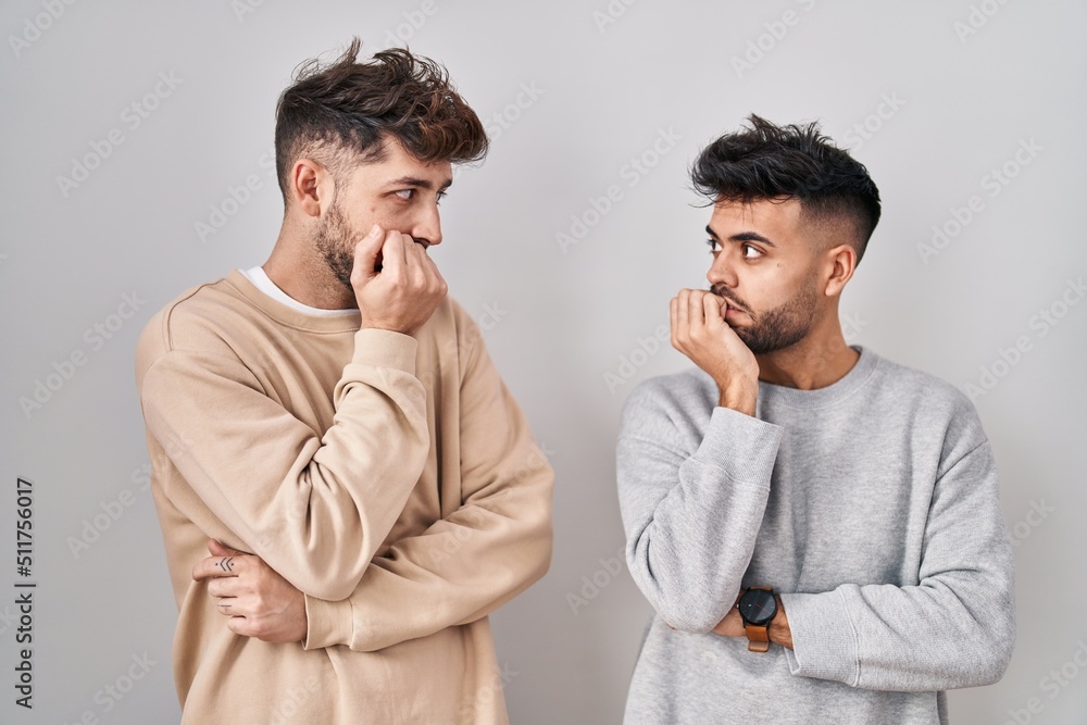 Young homosexual couple standing over white background looking stressed and nervous with hands on mouth biting nails. anxiety problem. Young homosexual couple standing over white background looking stressed and nervous with hands on mouth biting nails. anxiety problem.