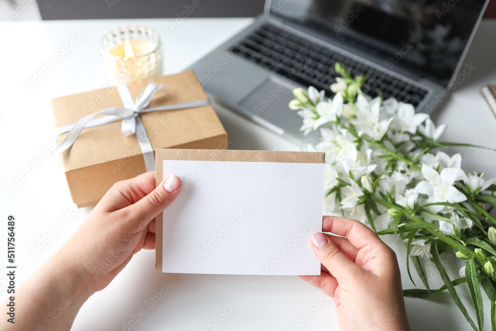 Woman holding envelope with blank greeting card, gift and flowers on the desktop Woman holding envelope with blank greeting card, gift and flowers on the desktop