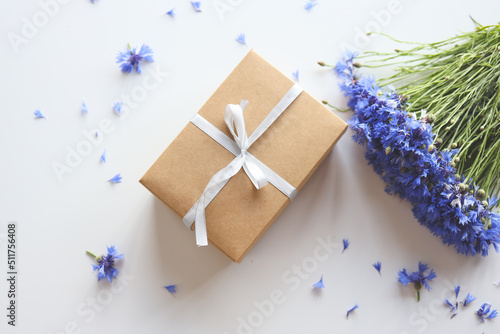 Bouquet of beautiful cornflowers and gift box on light table, flat lay. Space for text