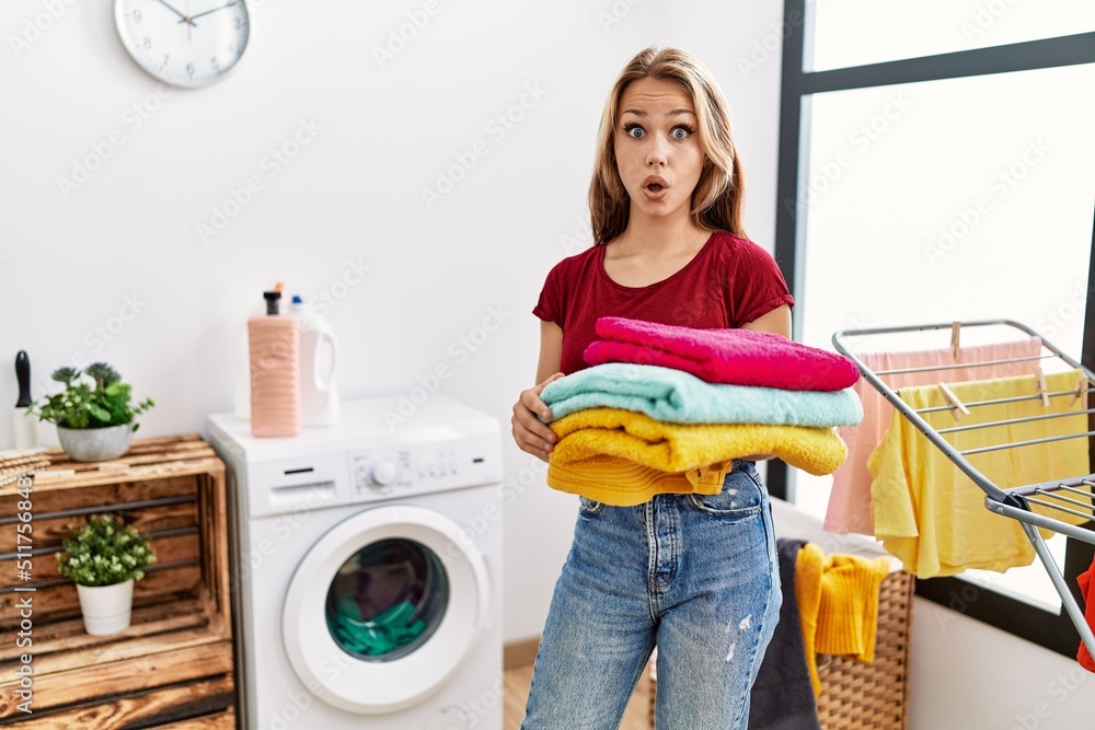 Young caucasian woman holding clean laundry scared and amazed with open mouth for surprise, disbelief face Young caucasian woman holding clean laundry scared and amazed with open mouth for surprise, disbelief face