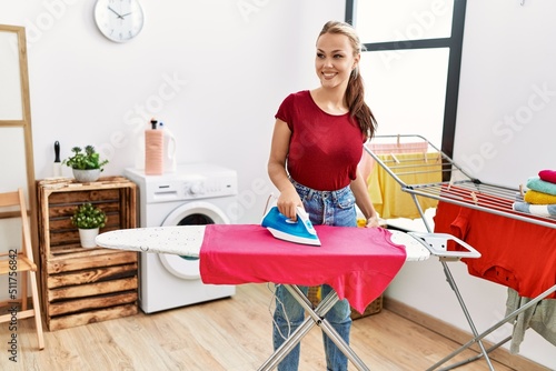 Young caucasian girl smiling happy ironing clothes at home.