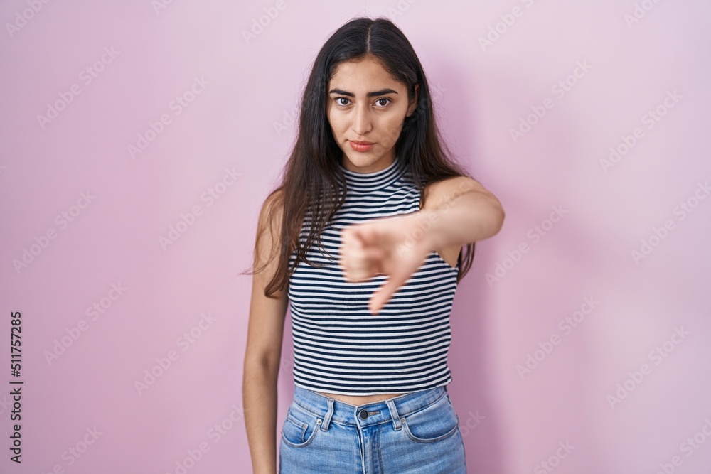 Young teenager girl wearing casual striped t shirt looking unhappy and angry showing rejection and negative with thumbs down gesture. bad expression. Young teenager girl wearing casual striped t shirt looking unhappy and angry showing rejection and negative with thumbs down gesture. bad expression.