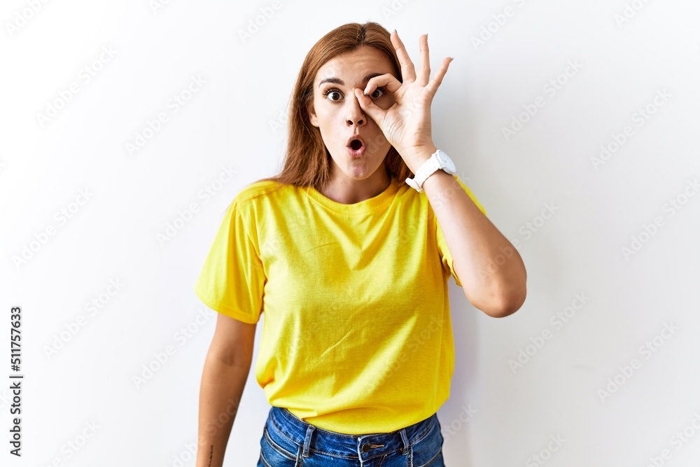 Young brunette woman standing over isolated background doing ok gesture shocked with surprised face, eye looking through fingers. unbelieving expression. Young brunette woman standing over isolated background doing ok gesture shocked with surprised face, eye looking through fingers. unbelieving expression.