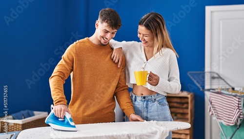 Young man and woman couple ironing clothes drinking coffee at laundry room