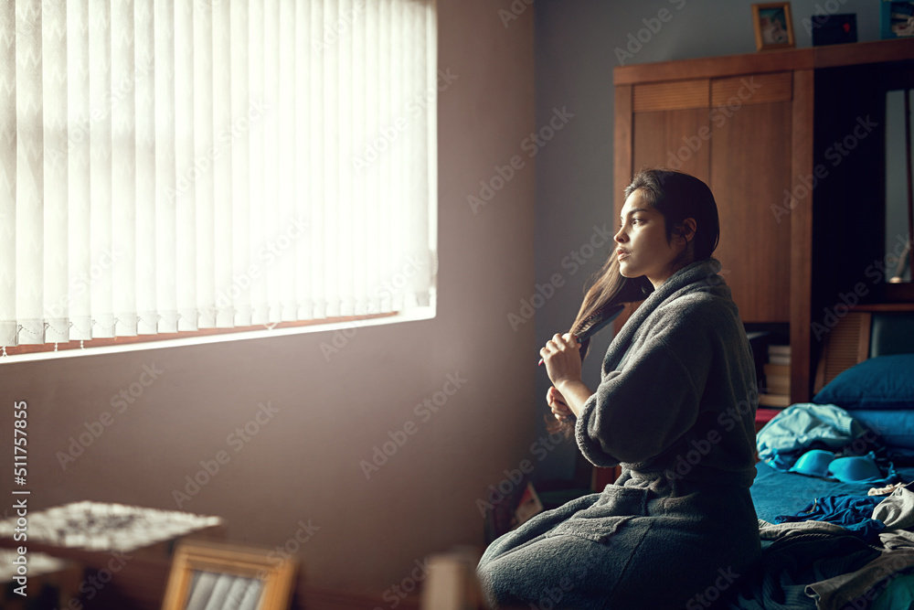 Thinking about the day that lies ahead. Shot of a young woman brushing her hair while sitting on her bed in the morning. Thinking about the day that lies ahead. Shot of a young woman brushing her hair while sitting on her bed in the morning.
