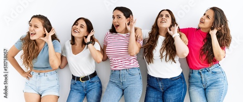 Group of women wearing casual clothes standing over isolated background smiling with hand over ear listening an hearing to rumor or gossip. deafness concept. photo