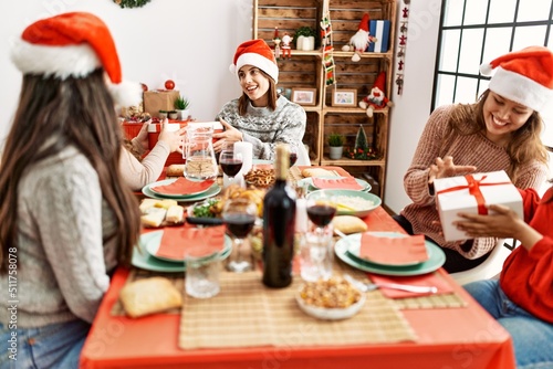 Group of young hispanic women having christmas dinner and giving gifts sitting on the table at home.