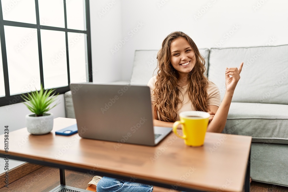 Beautiful hispanic woman using computer laptop at home smiling happy pointing with hand and finger to the side Beautiful hispanic woman using computer laptop at home smiling happy pointing with hand and finger to the side