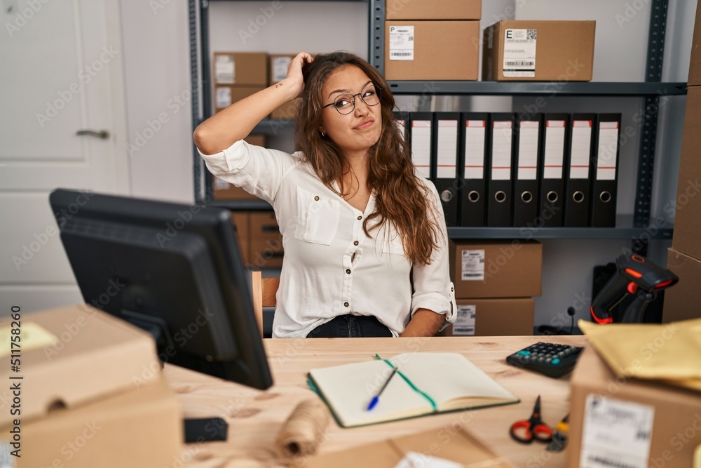 Young hispanic woman working at small business ecommerce confuse and wondering about question. uncertain with doubt, thinking with hand on head. pensive concept. Young hispanic woman working at small business ecommerce confuse and wondering about question. uncertain with doubt, thinking with hand on head. pensive concept.