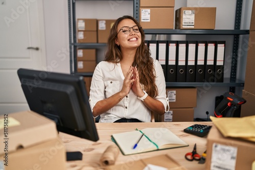 Young hispanic woman working at small business ecommerce hands together and fingers crossed smiling relaxed and cheerful. success and optimistic