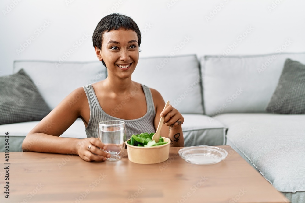 Young hispanic woman smiling confident eating salad at home