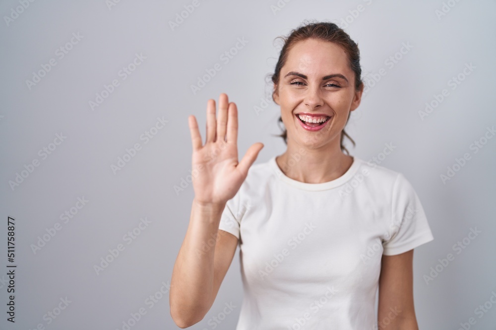 Beautiful brunette woman standing over isolated background waiving saying hello happy and smiling, friendly welcome gesture Beautiful brunette woman standing over isolated background waiving saying hello happy and smiling, friendly welcome gesture
