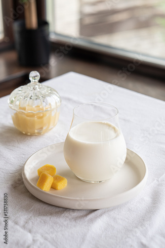 A glass of milk on a table with a white tablecloth. Glass jar with honey and yellow candies.