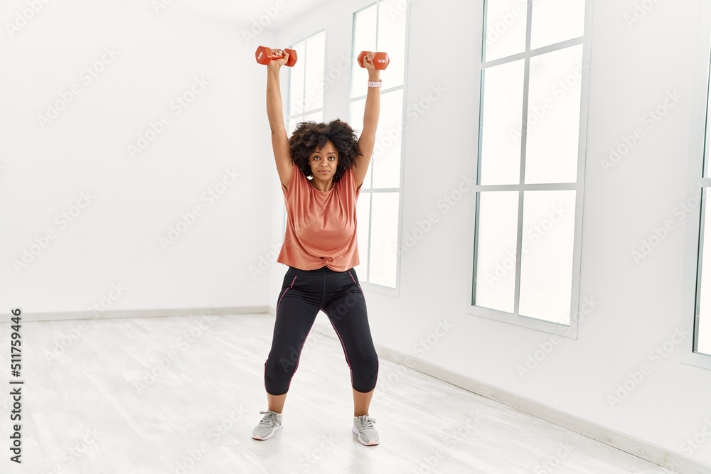 Young african american woman training using dumbbells at sport center Young african american woman training using dumbbells at sport center