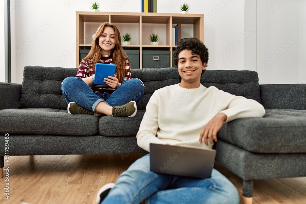 Young couple smiling happy using laptop and touchpad sitting on the sofa at home. Young couple smiling happy using laptop and touchpad sitting on the sofa at home.