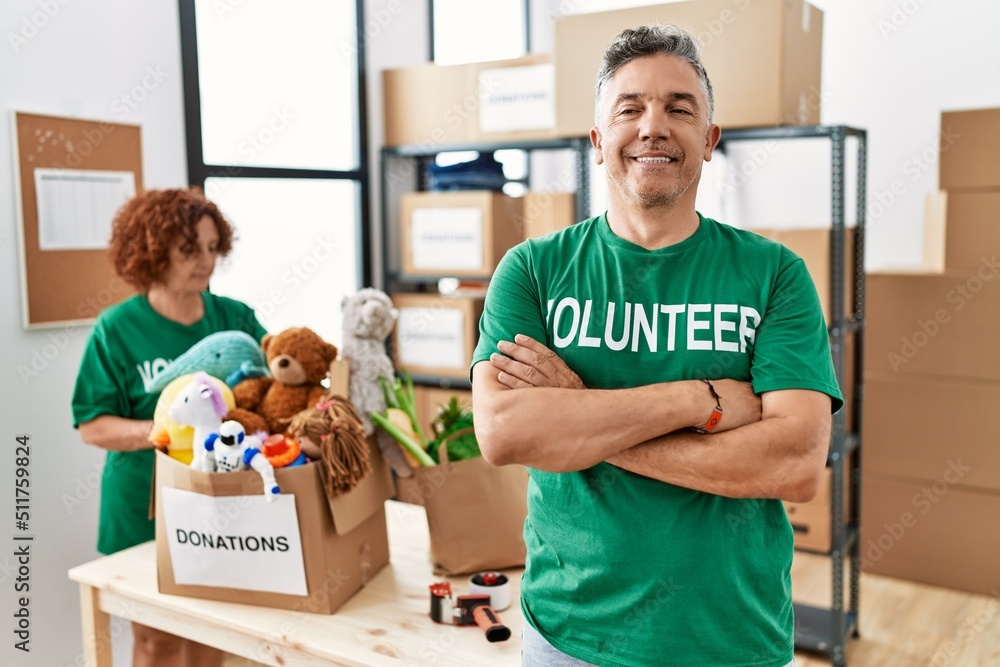 Middle age man wearing volunteer t shirt at donations stand happy face smiling with crossed arms looking at the camera. positive person. Middle age man wearing volunteer t shirt at donations stand happy face smiling with crossed arms looking at the camera. positive person.