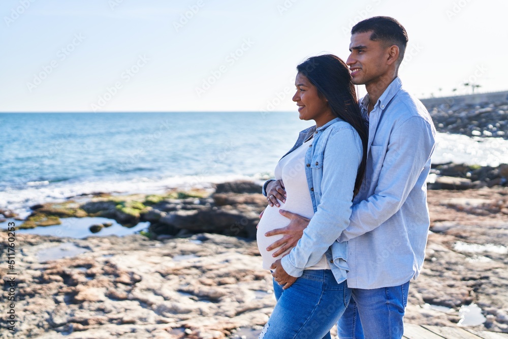 Young latin couple expecting baby hugging each other standing at seaside Young latin couple expecting baby hugging each other standing at seaside