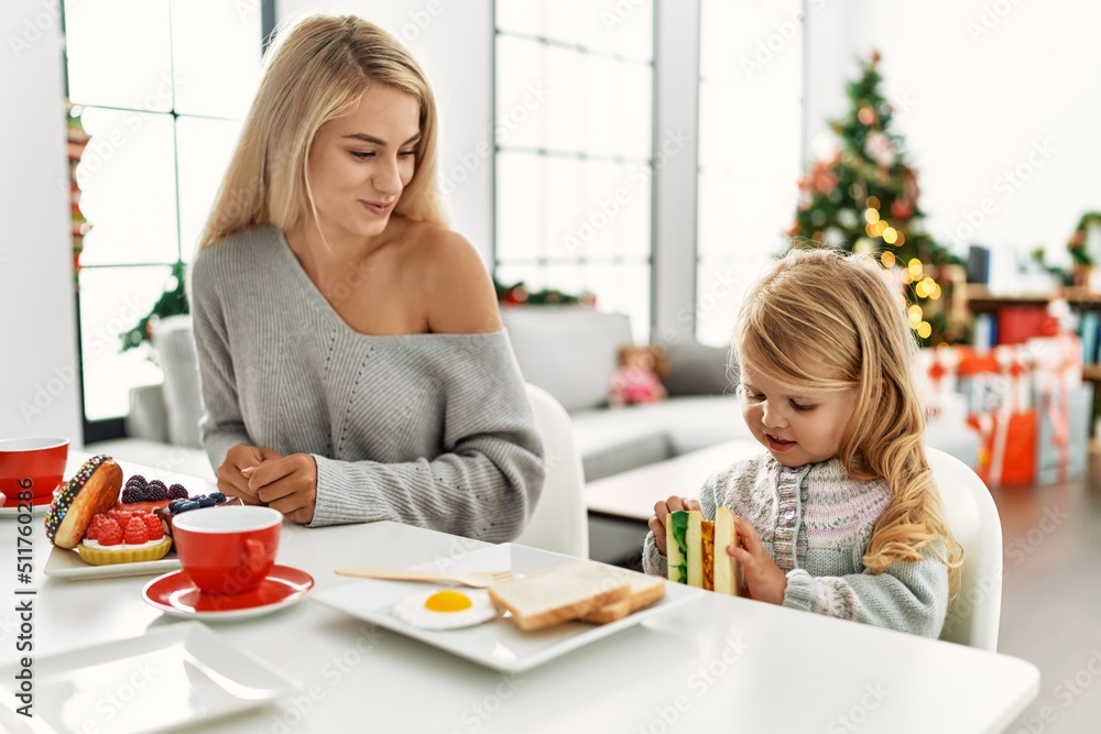 Mother and daughter having breakfast sitting by christmas tree at home