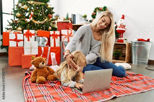 Mother and daughter using laptop sitting by christmas tree at home