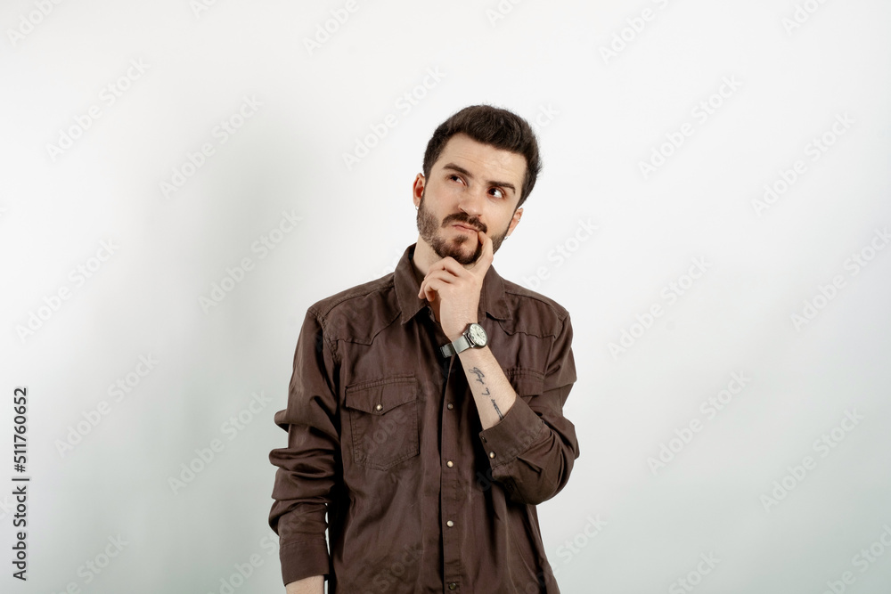 Caucasian man wearing brown shirt posing isolated over white background looking at upper right corner touching lip, thinking. Trying think up solution. Caucasian man wearing brown shirt posing isolated over white background looking at upper right corner touching lip, thinking. Trying think up solution.