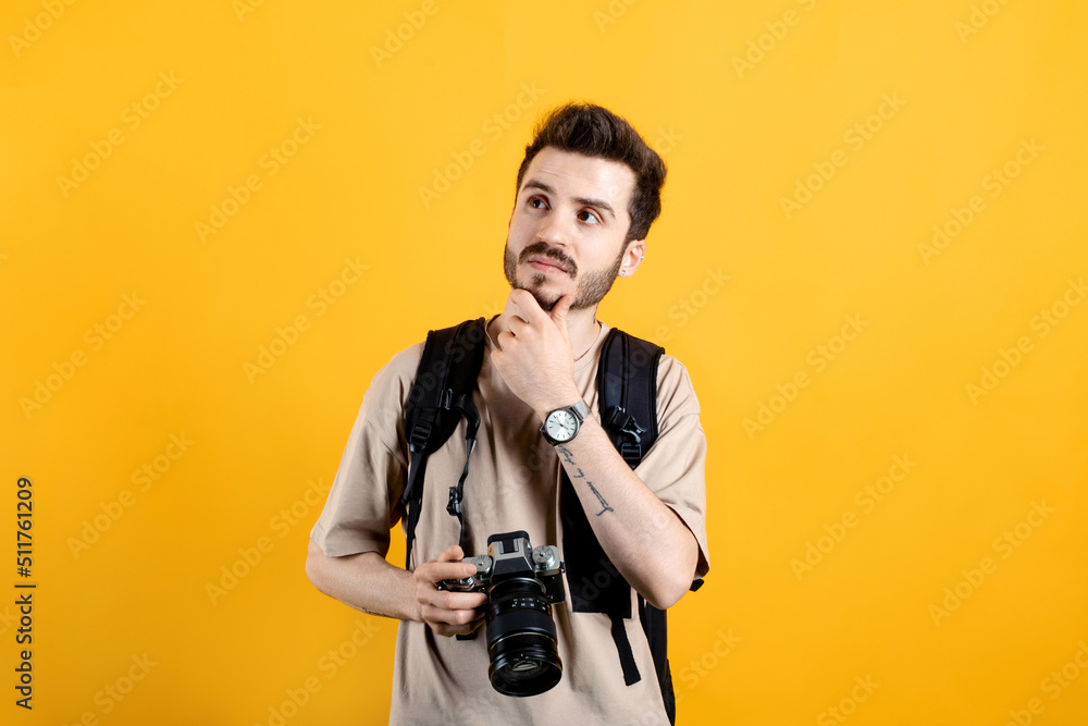 Handsome caucasian man wearing beige t-shirt posing isolated over yellow background serious face thinking about question, very confused idea while holding a dslr camera. Handsome caucasian man wearing beige t-shirt posing isolated over yellow background serious face thinking about question, very confused idea while holding a dslr camera.