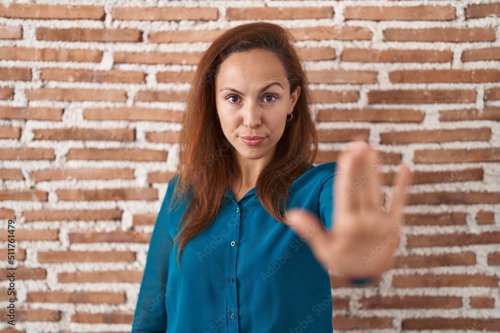 Brunette woman standing over bricks wall doing stop sing with palm of the hand. warning expression with negative and serious gesture on the face. Brunette woman standing over bricks wall doing stop sing with palm of the hand. warning expression with negative and serious gesture on the face.