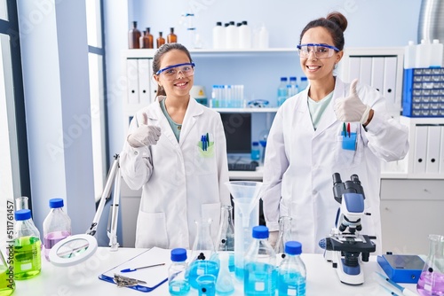 Young mother and daughter at scientist laboratory smiling happy and positive  thumb up doing excellent and approval sign