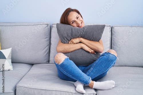 Young woman hugging cushion sitting on sofa at home