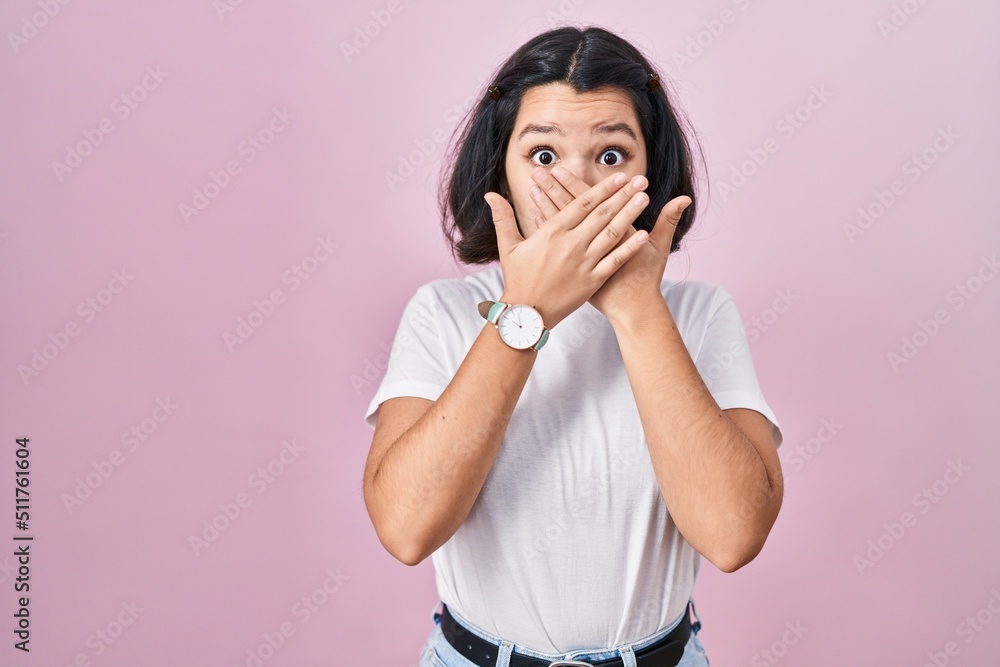 Young hispanic woman wearing casual white t shirt over pink background shocked covering mouth with hands for mistake. secret concept. Young hispanic woman wearing casual white t shirt over pink background shocked covering mouth with hands for mistake. secret concept.