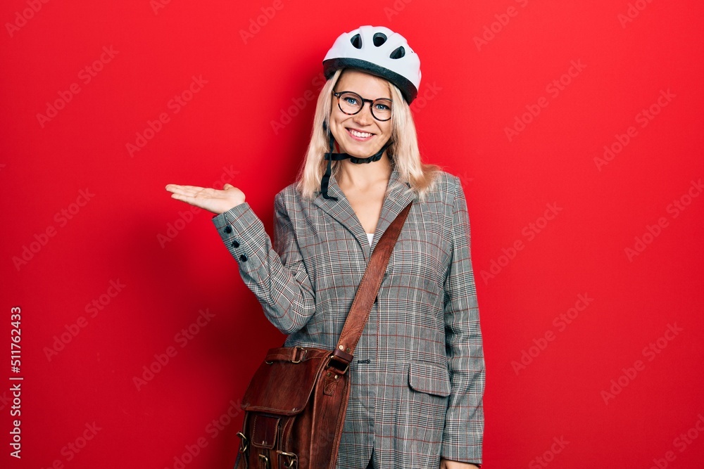 Fototapeta premium Beautiful caucasian blonde business woman wearing bike helmet smiling cheerful presenting and pointing with palm of hand looking at the camera.