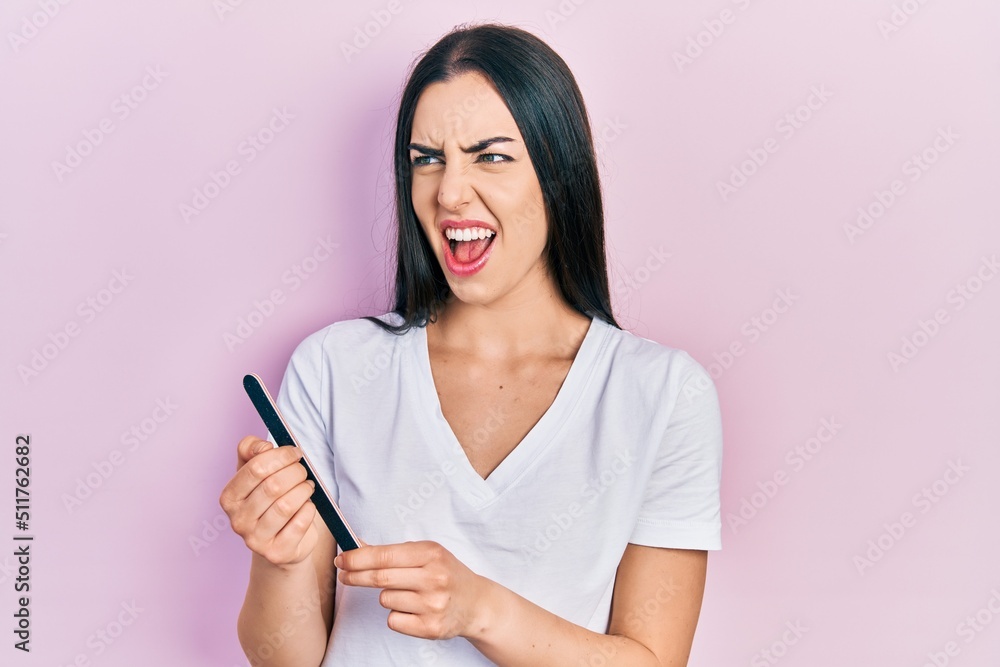 Beautiful woman with blue eyes using file nail angry and mad screaming frustrated and furious, shouting with anger. rage and aggressive concept. Beautiful woman with blue eyes using file nail angry and mad screaming frustrated and furious, shouting with anger. rage and aggressive concept.